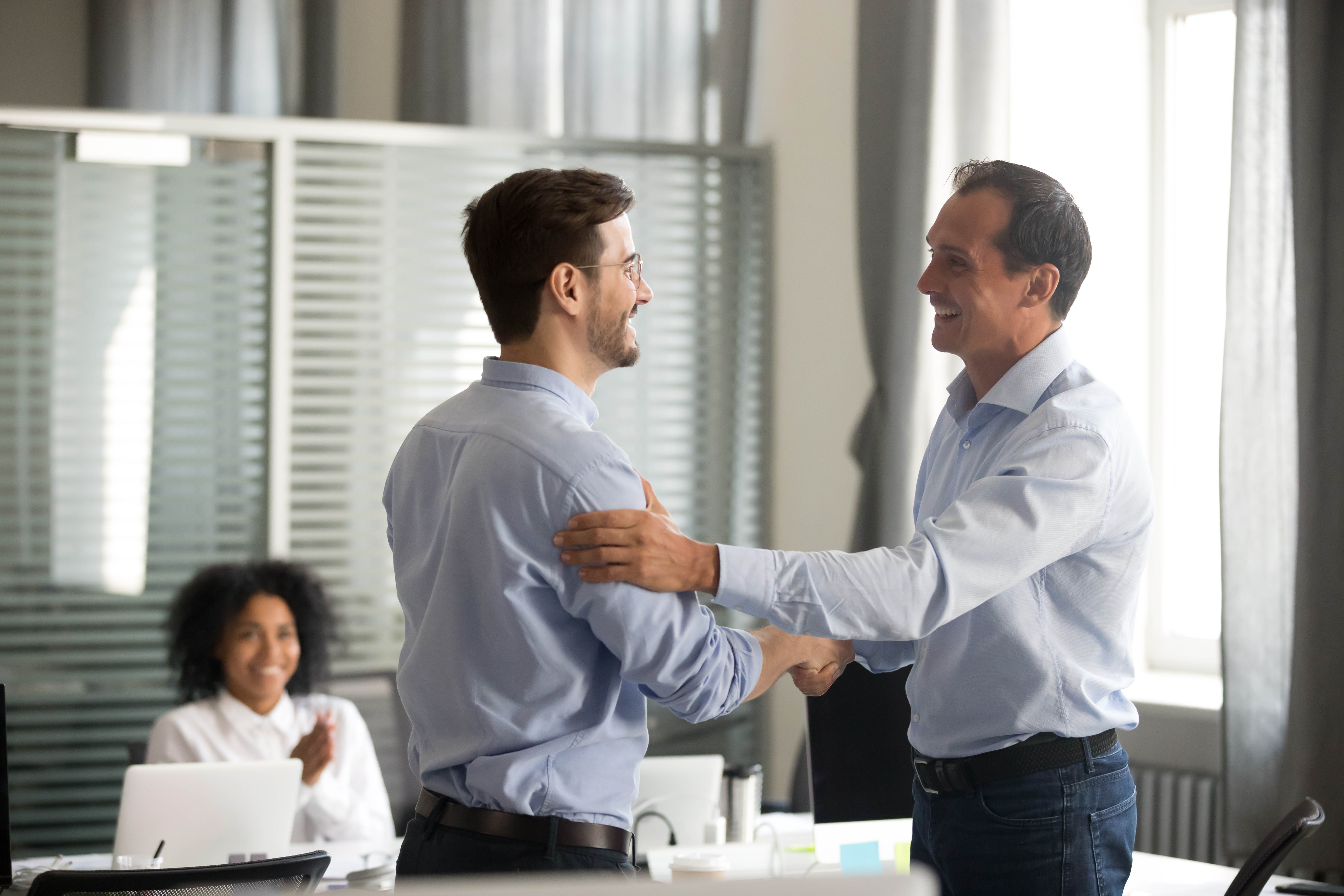 Male boss showing support and appreciation for his male colleague with a hand on his back and handshake in a meeting room Male boss showing support and appreciation for his male colleague with a hand on his back and handshake in a meeting room